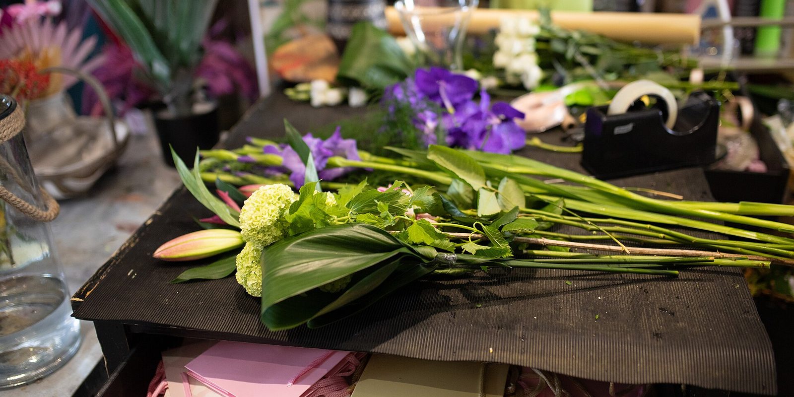 Cut stems and green foliage laid on a florist's workbench beside a tape dispenser and glass vases