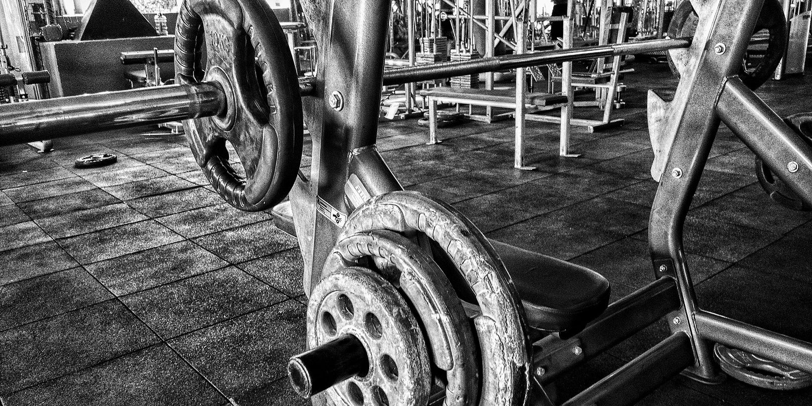 Black and white view of a loaded barbell and weight plates on a bench rack in an empty gym