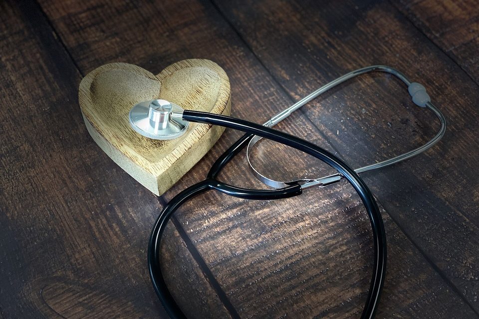 A stethoscope resting against a small carved wooden heart on dark weathered planks