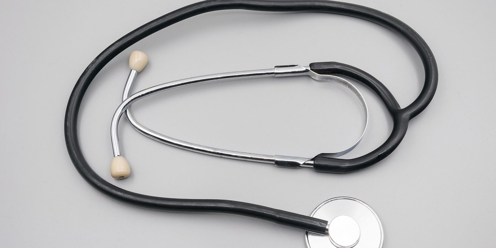 A black stethoscope coiled on a plain light grey surface, chest piece at lower right