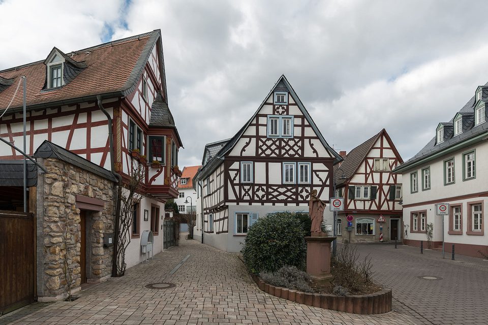 A cobbled village square lined with old timber framed houses under a grey sky