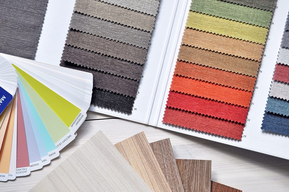 Fabric swatch books in greens, browns and reds beside a paint fan deck and wood veneer samples