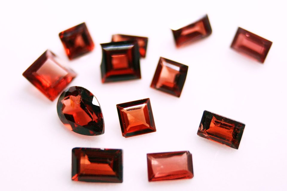 Twelve loose deep red garnets, cut as squares, rectangles and one pear, on a white surface