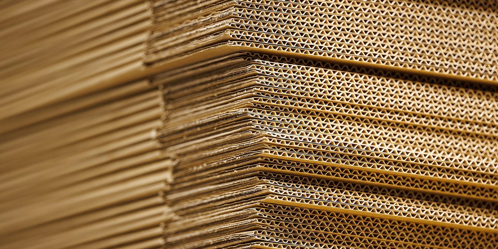 Close view of a tall stack of flat corrugated cardboard sheets showing their fluted edges