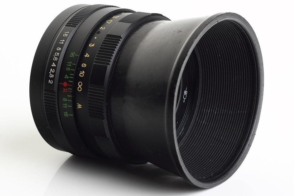 A black manual camera lens on a white background, aperture and focus rings marked in colour
