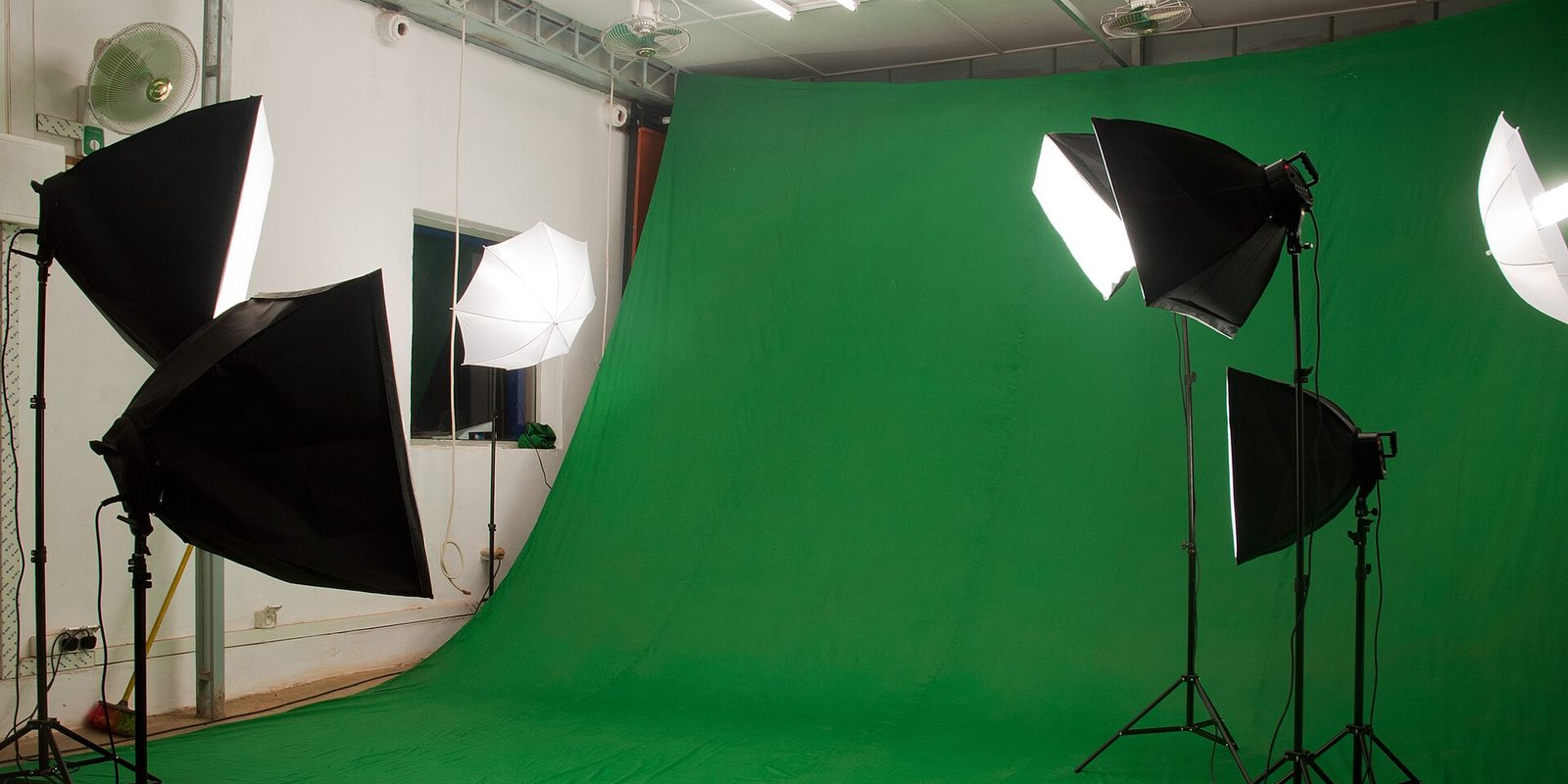 An empty photo studio with a green backdrop, softboxes and a white umbrella on stands