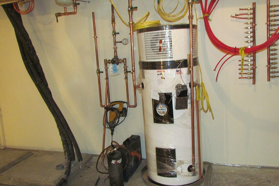 A basement water heater surrounded by copper pipes, valves and red and yellow manifold lines