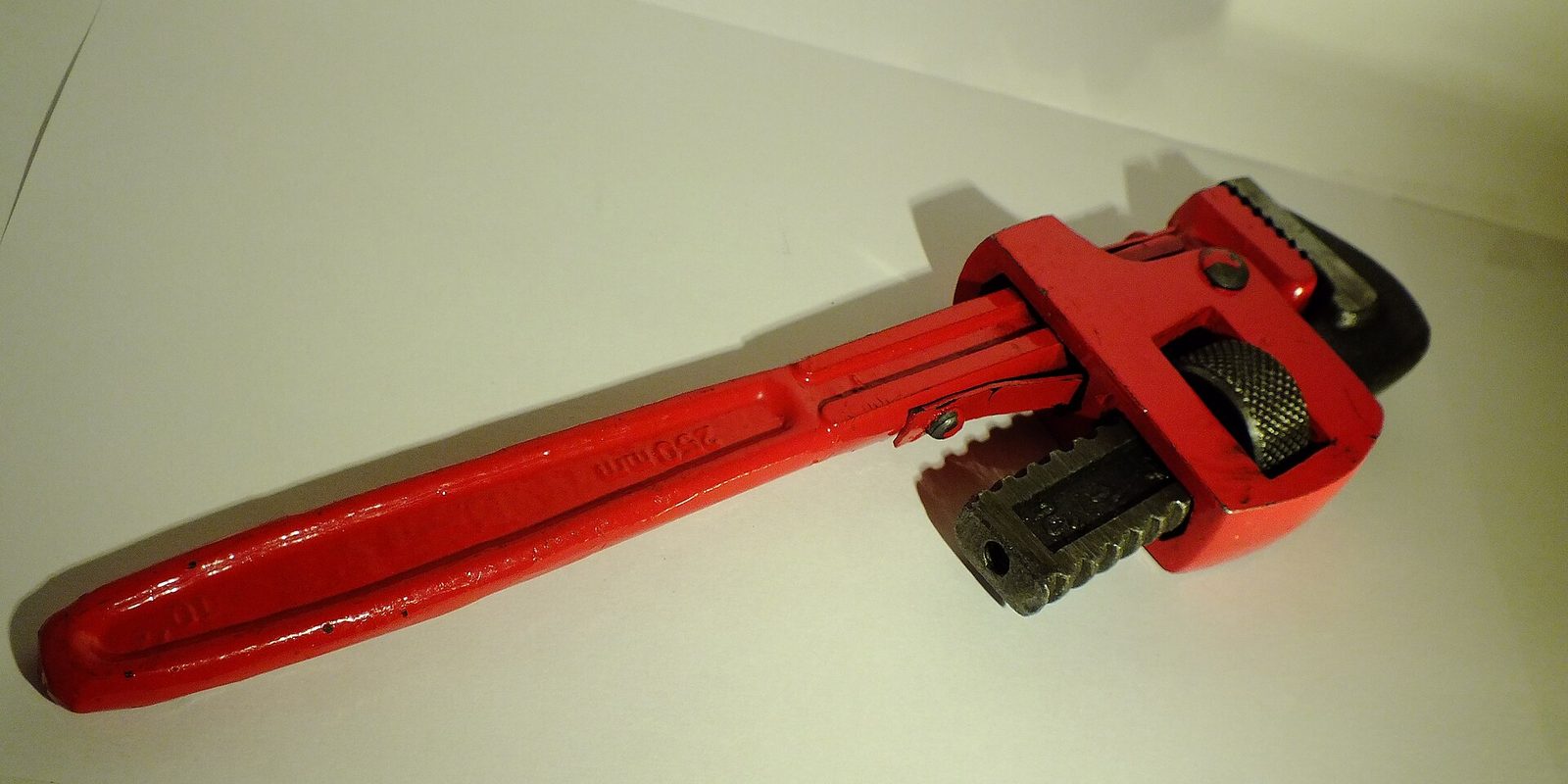 A red adjustable pipe wrench lying on a plain white surface