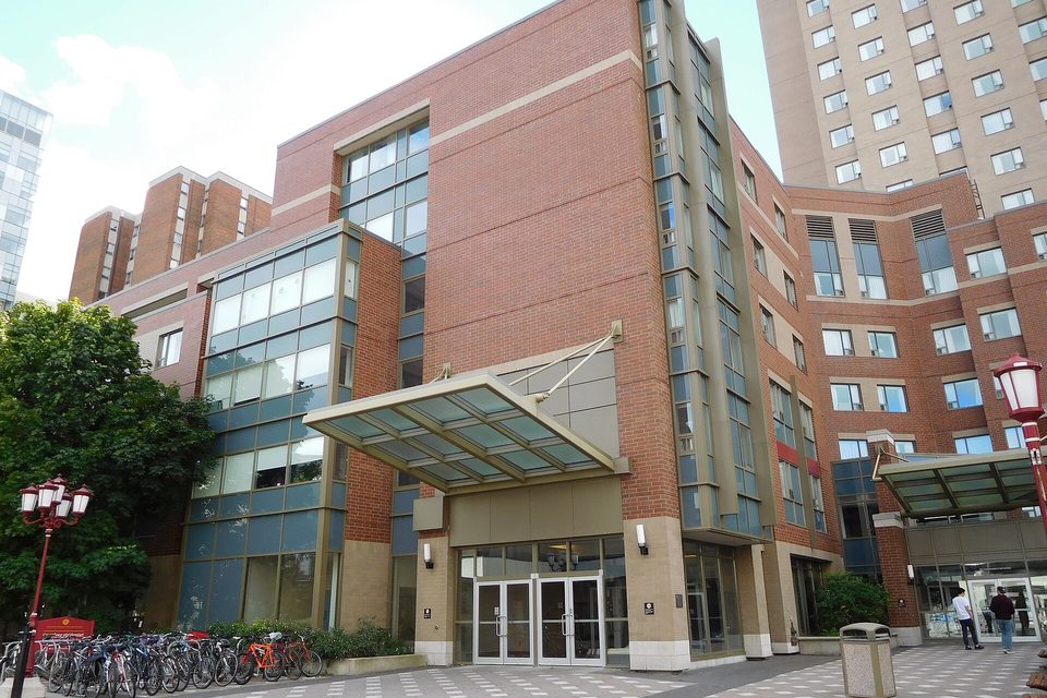 Brick apartment building entrance with a glass canopy, double doors and a rack of parked bicycles