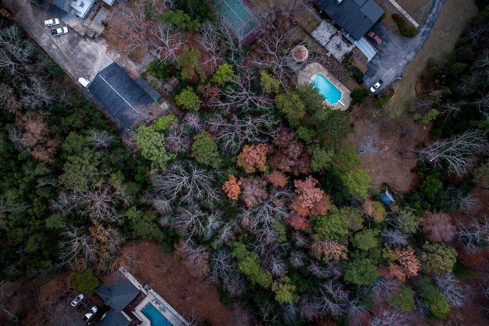 Overhead aerial view of wooded houses with swimming pools, driveways and a tennis court