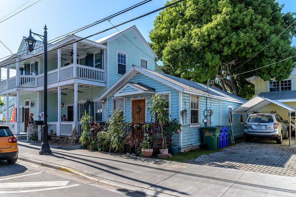 Pale blue wood-sided houses with covered porches along a sunny residential street