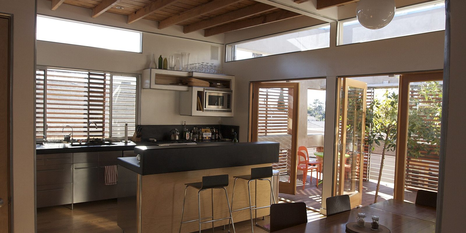 Open plan kitchen with a black island, bar stools and timber beams opening onto a patio
