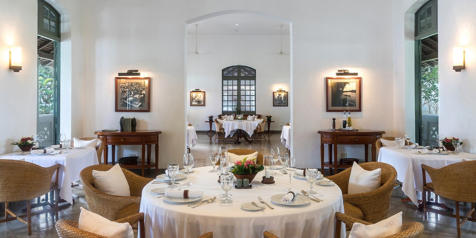 Empty white-walled dining room with linen-covered tables, wicker armchairs and framed pictures