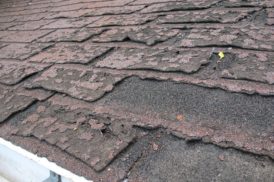 Close view of an aging asphalt shingle roof with cracked, curled and missing shingles above a gutter