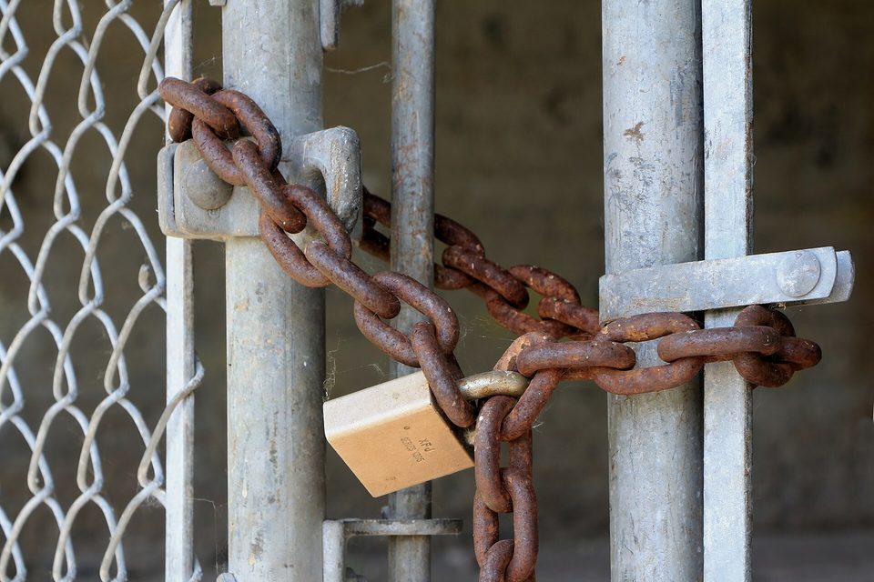 A rusted chain and brass padlock holding a galvanised chain link gate shut