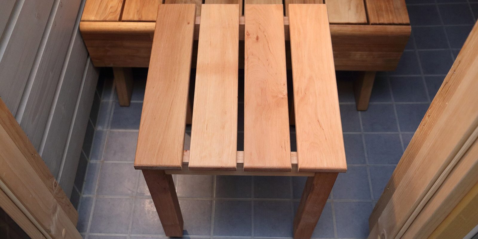 Two slatted wooden benches on blue-grey tiles inside a small cedar-lined sauna room