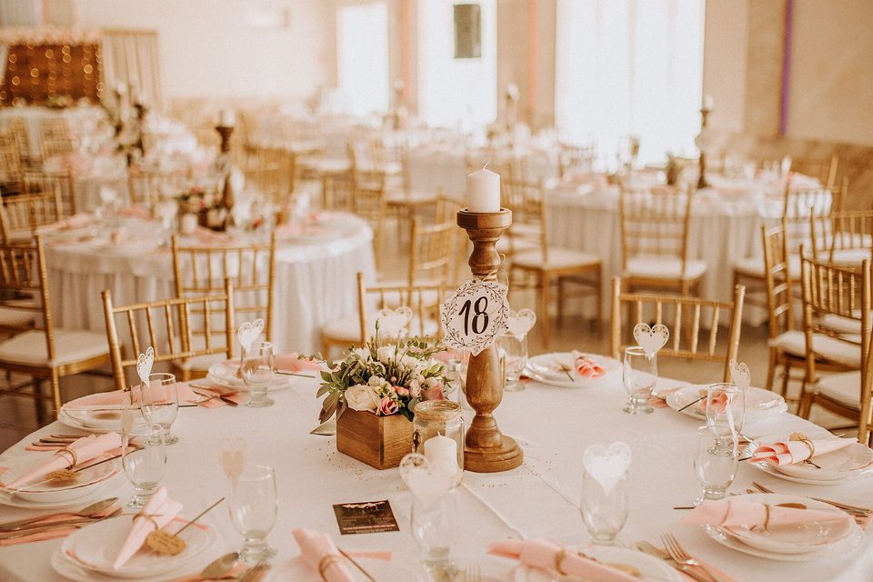 A round banquet table set with pink napkins, glassware and a candle centrepiece in a reception hall