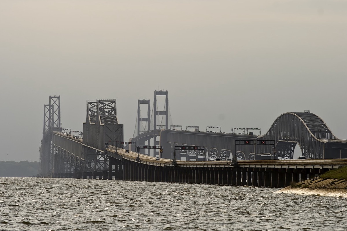 The long steel spans of the Chesapeake Bay crossing in Maryland receding into grey haze, the near piers standing in choppy water and a low green shore at the right hand end.