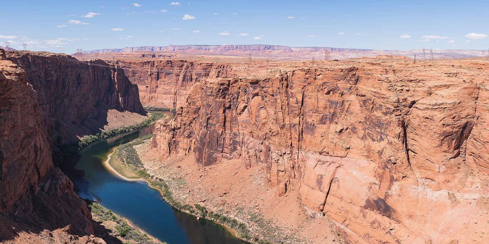 A green river winding through a deep red sandstone canyon under a pale blue sky