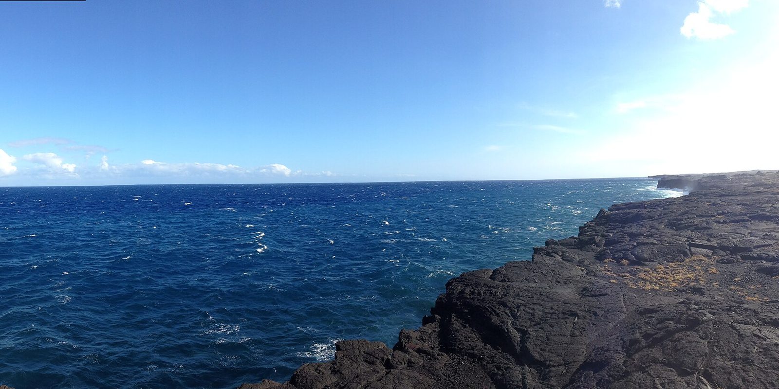Dark volcanic rock shelf dropping into choppy deep blue ocean under a clear sky