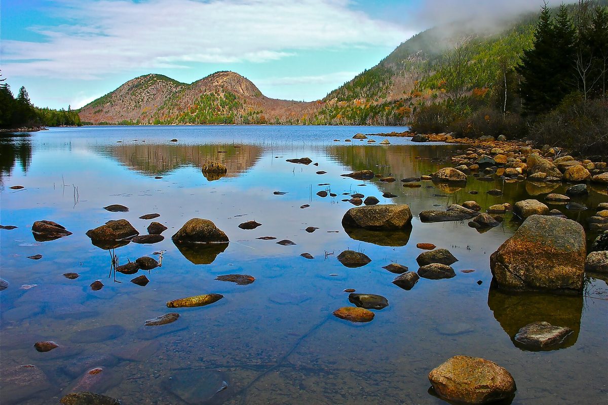The Bubbles rising above Jordan Pond in Acadia, Maine, with granite boulders in the clear shallows and autumn color on the slopes.