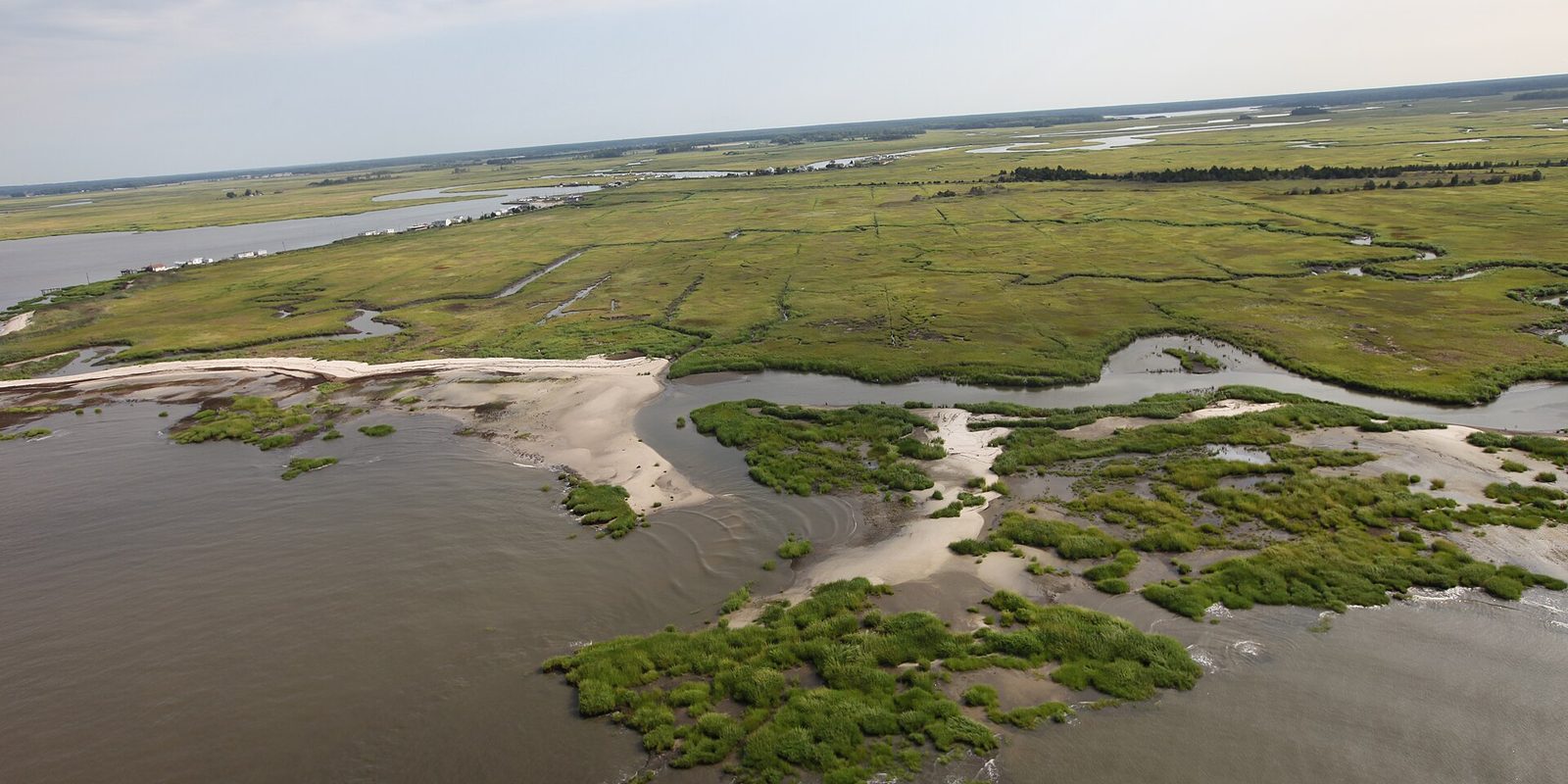 Aerial look across a coastal salt marsh, with sandbars, tidal channels and grassy flats meeting open water.