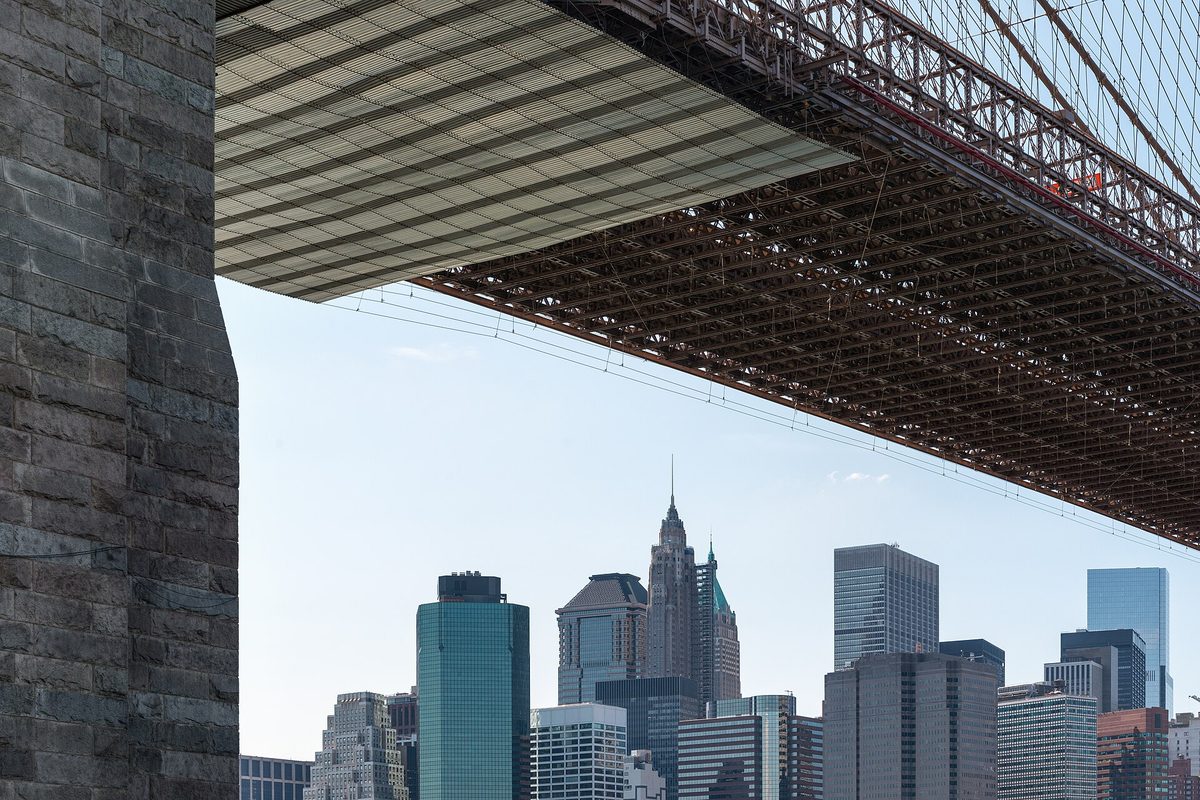 New York: the granite tower and steel underdeck of the Brooklyn Bridge frame the Lower Manhattan skyline.