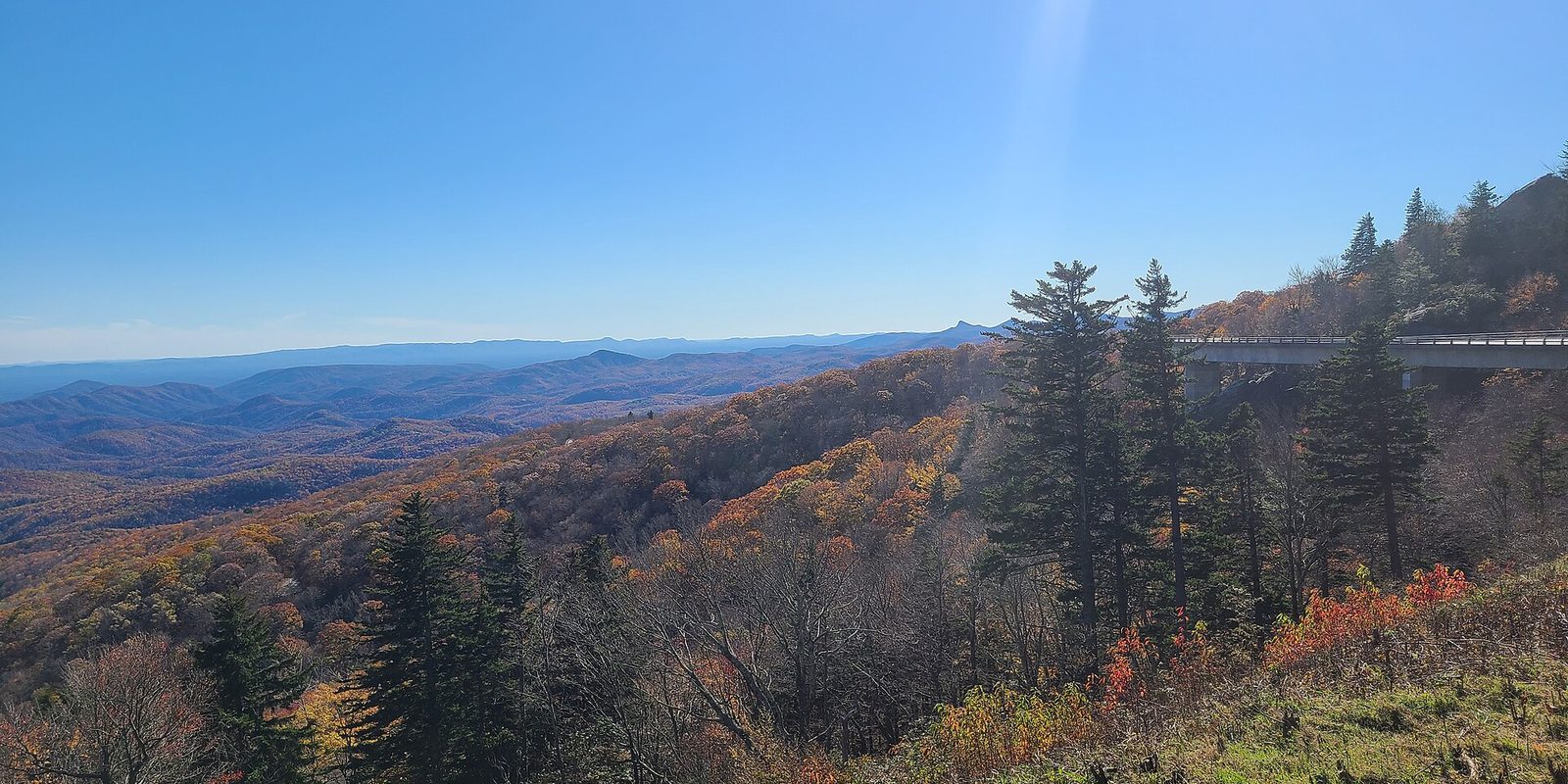Autumn forested ridges fading into blue haze, with a curving concrete viaduct along the right slope