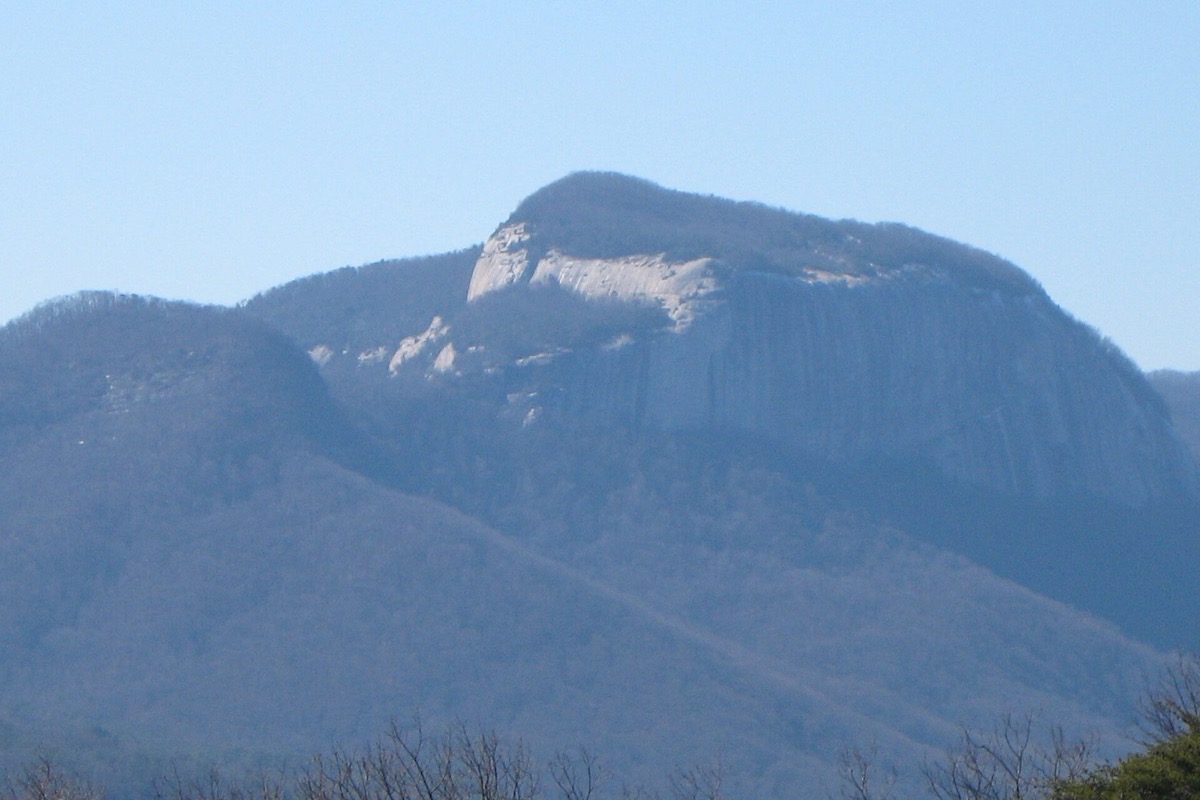 A flat topped granite dome standing above a wooded South Carolina valley, its bare grey face catching the light with forested slopes falling away on either side through blue haze.