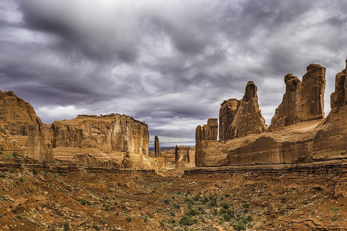 Utah red rock desert, where towering sandstone fins and monoliths flank a sagebrush wash beneath heavy gray storm clouds.
